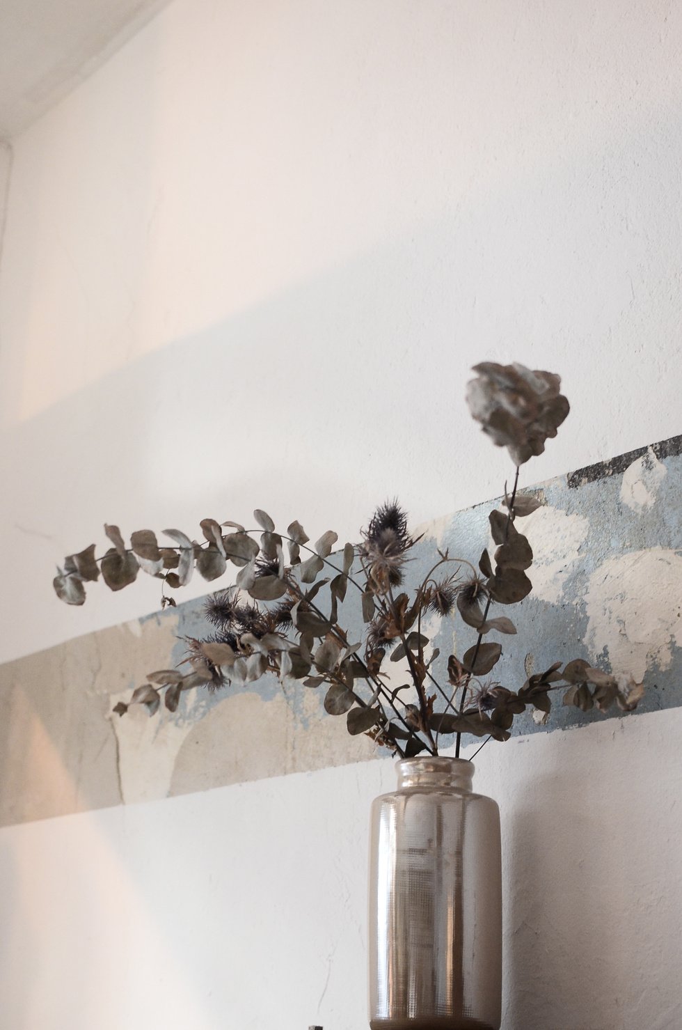 Vase with dried plants near wall in house